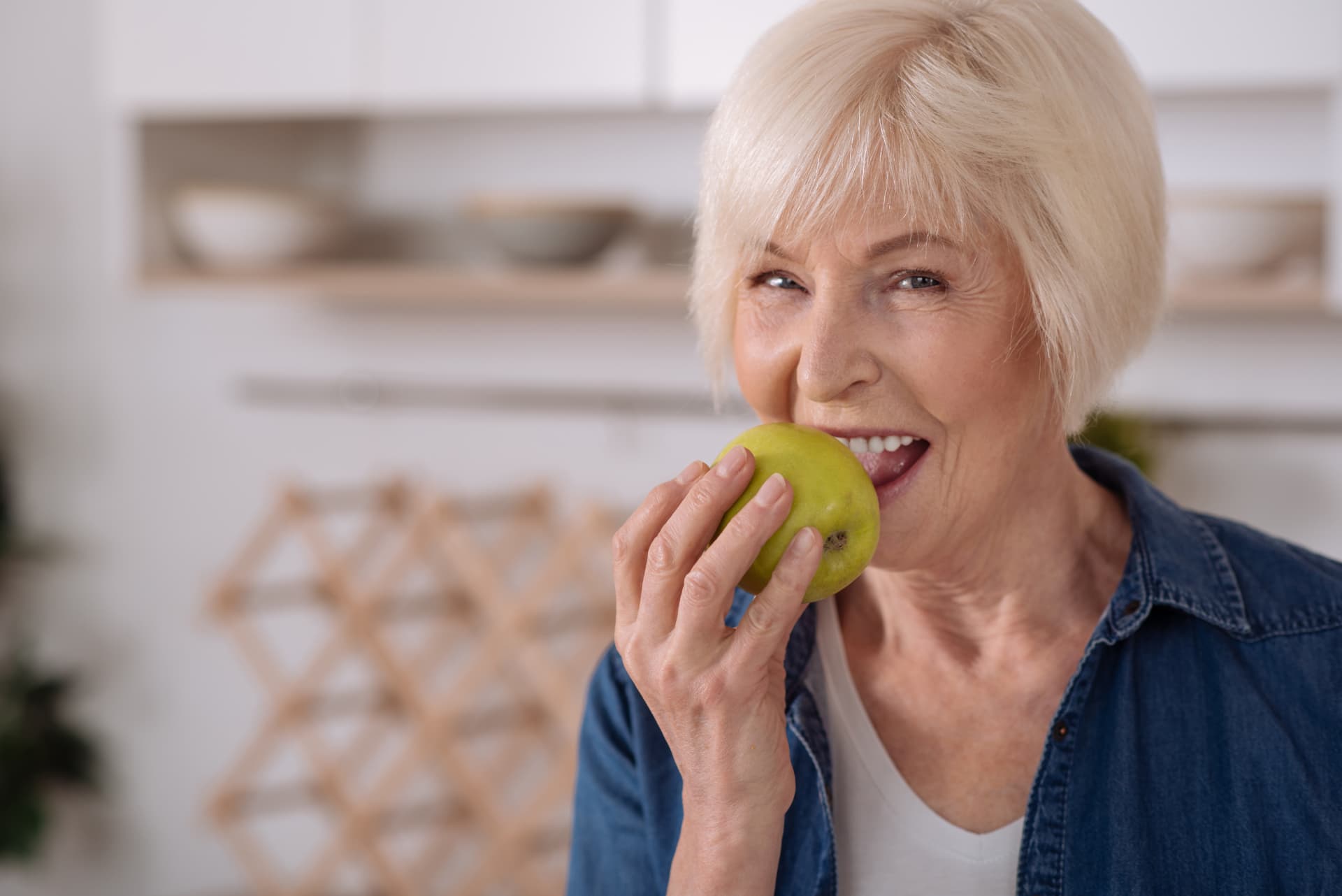Older woman confidently biting into a crisp green apple after stabilizing her lower denture with mini dental implants