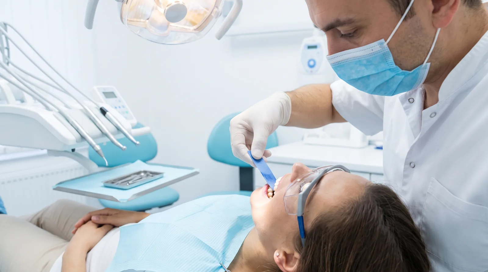 Patient in a dental chair while the dentist checks the bite on a healing temporary bridge with articulating paper