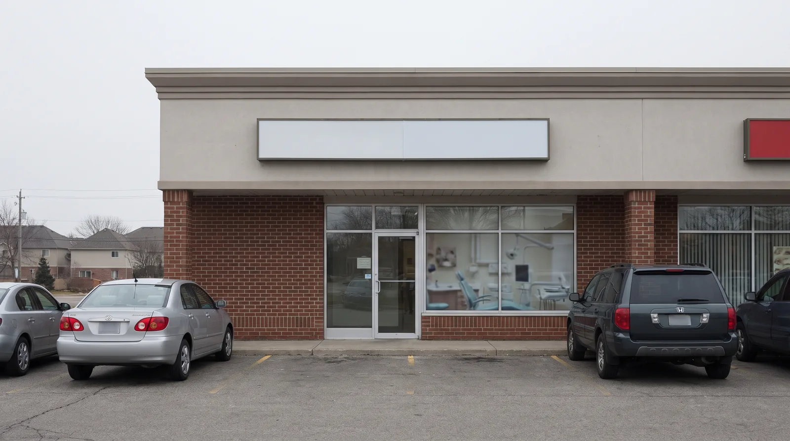 Suburban strip-mall dental office storefront in flat daylight, signage area left blank, a few cars in the lot
