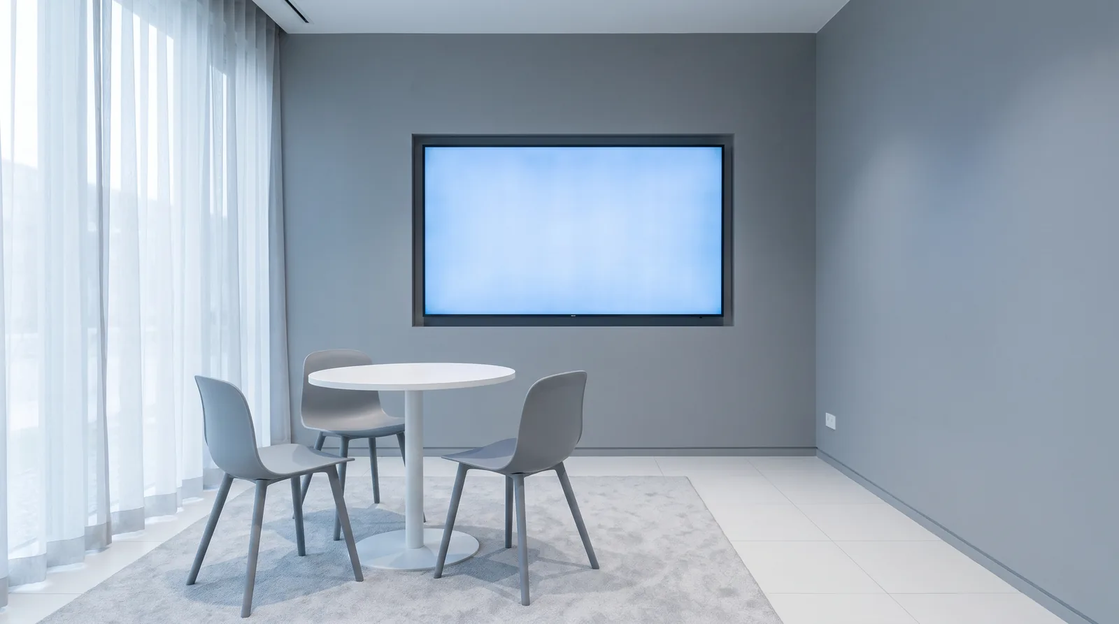 Consultation room with a large monitor, a conference-style table, and two chairs, empty and brightly lit