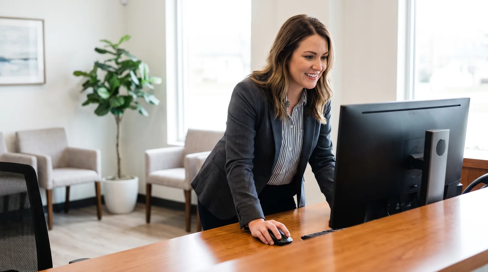 Practice manager at a front desk updating a listing on a desktop computer, screen angled away, tidy office