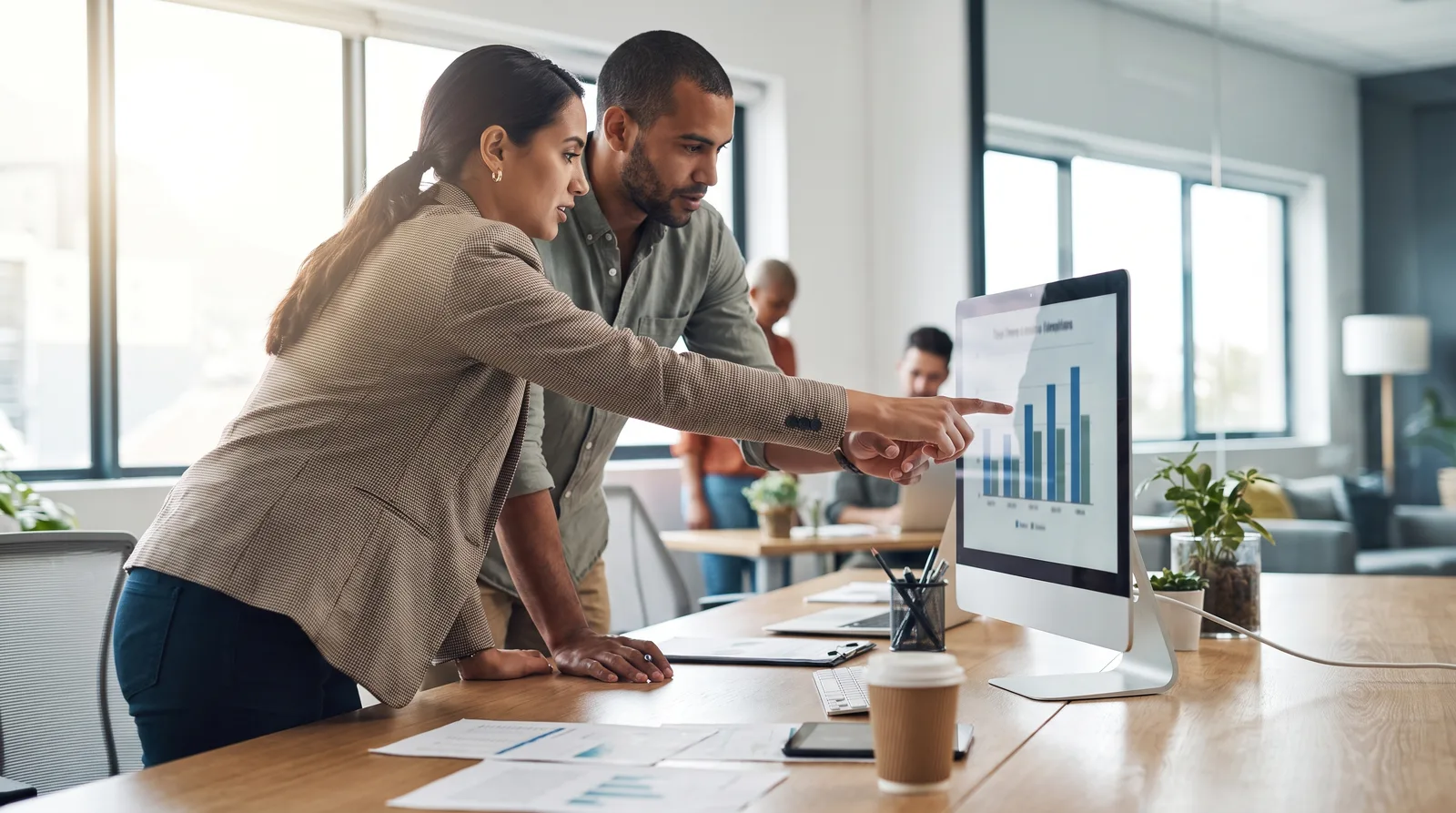 Practice owner and marketer reviewing a conversion report on a monitor, chart bars visible but labels blurred