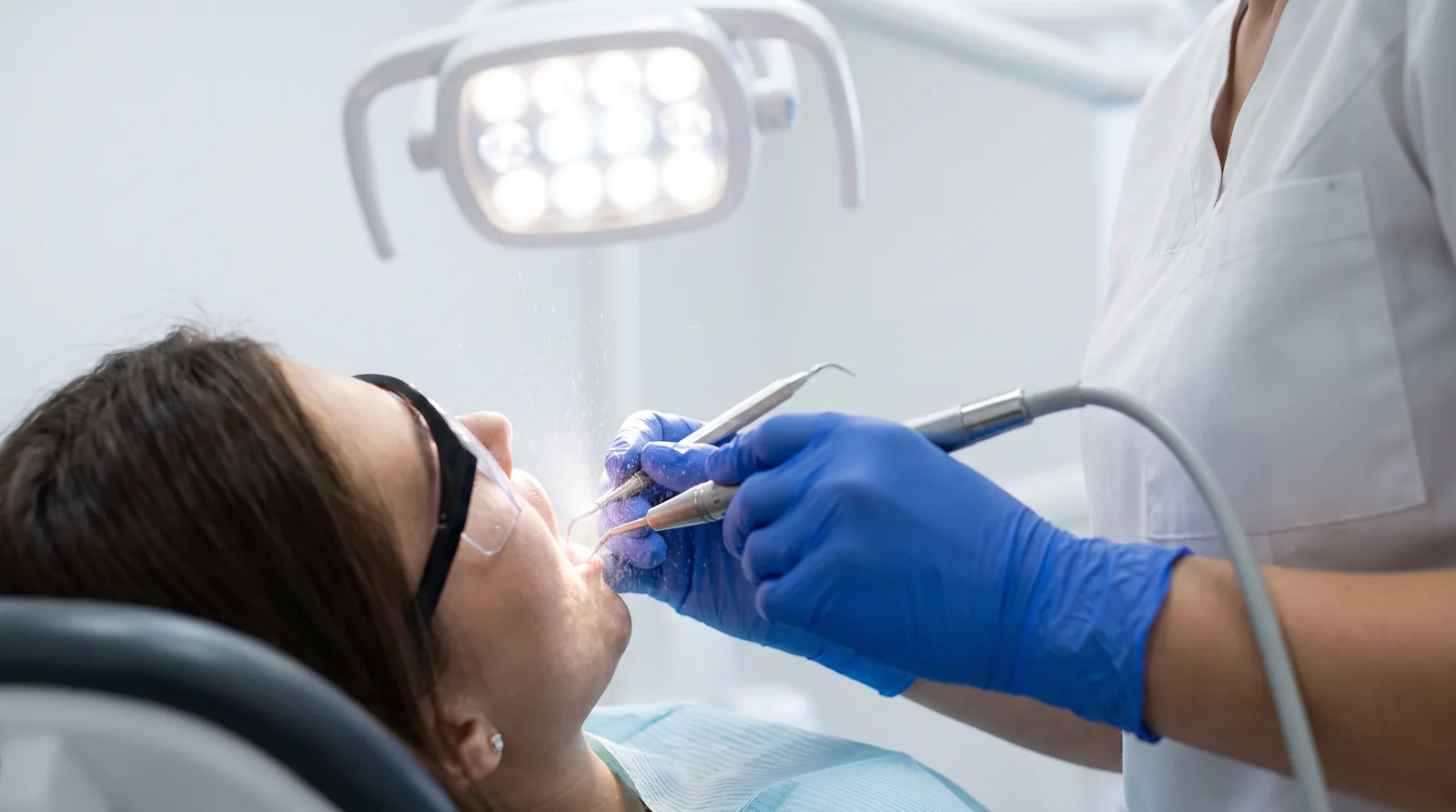 Dental hygienist performing a deep cleaning with an ultrasonic scaler on a patient, gloved hands, bright light