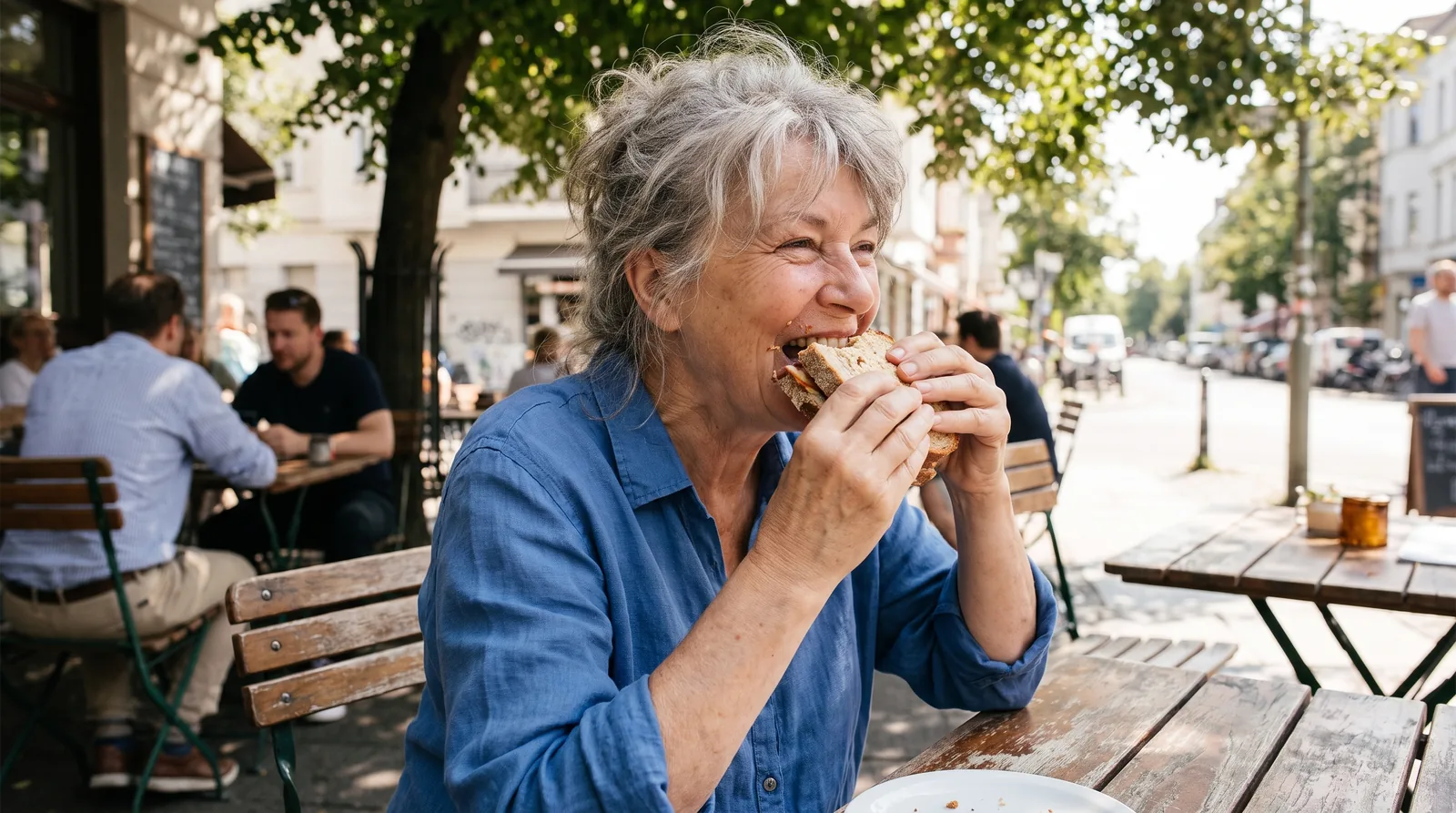 Older woman smiling while eating at a cafe table, relaxed, natural light, denture stable and unremarkable