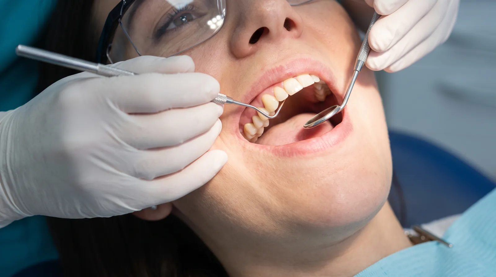 Dentist examining the gum around a single implant crown with a probe and mirror, patient reclined, close view