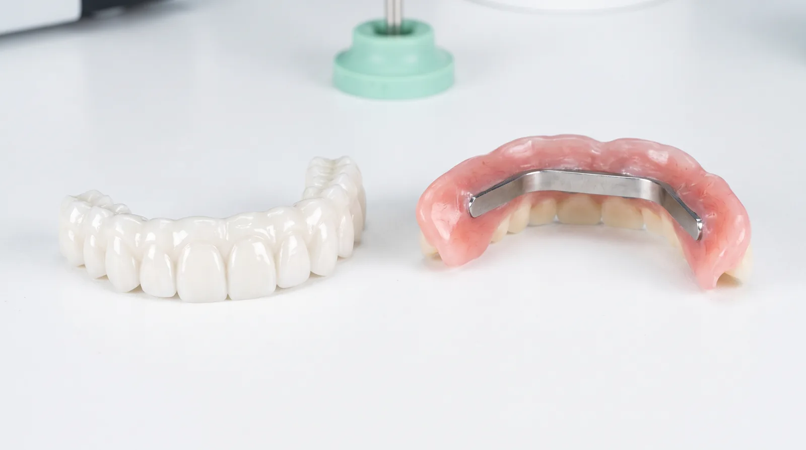 Zirconia and acrylic full-arch implant bridges side by side on a dental lab bench under bright light